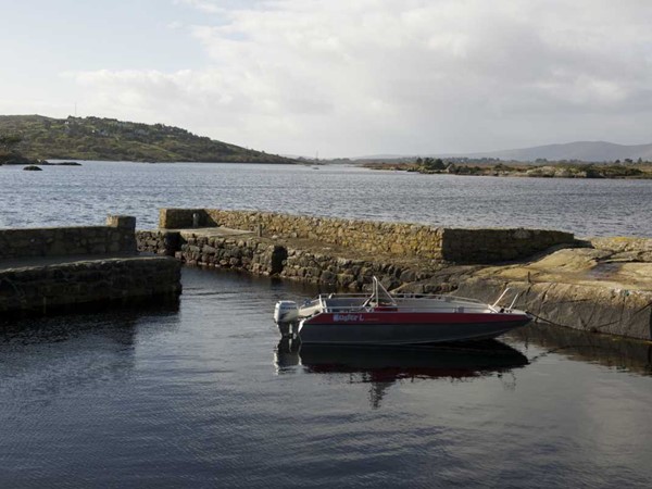 A small boat moored at a stone pier on Camus Bay, with the Connemara coastline beyond